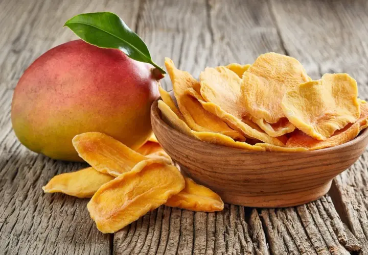 Un mango fresco e una ciotola di mango disidratato, che ne esaltano le proprietà nutritive e il sapore concentrato.
