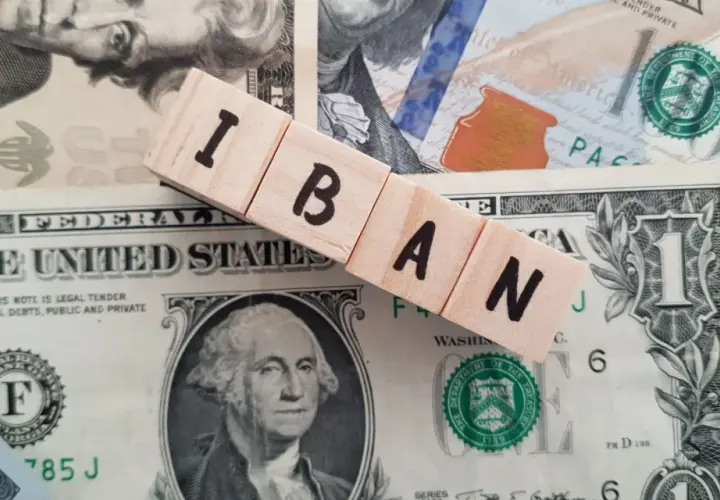 Drewniane klocki z literami IBAN leżą na banknotach dolarowych.