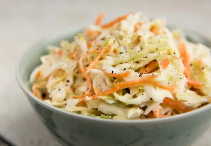 En skål med krämig, krispig coleslaw med strimlad vitkål och morötter, toppad med svartpeppar. Perfekt som tillbehör till grillat, detta är den godaste coleslaw!