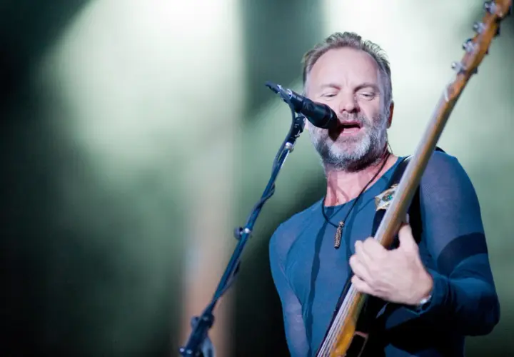 Sting, wokalista The Police, gra na gitarze basowej i śpiewa do mikrofonu na koncercie.