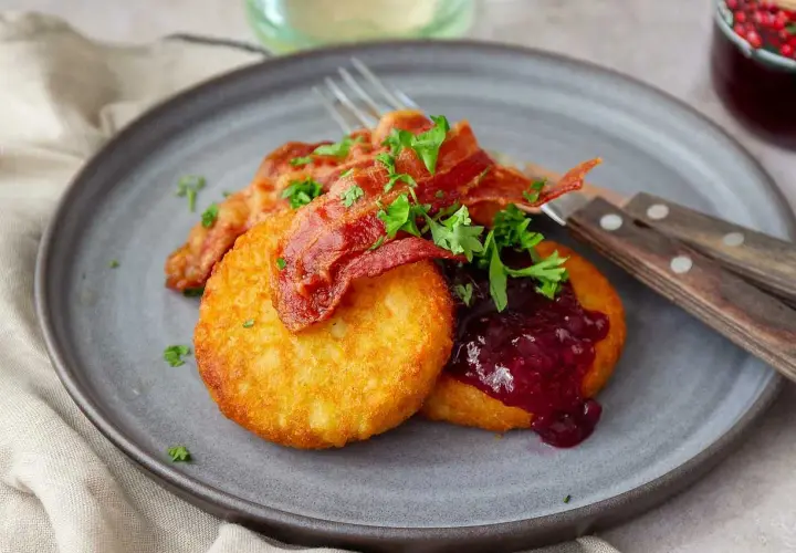 Gylla potatisbullar airfryer med knaprigt bacon, lingonsylt och persilja på en grå tallrik. En klassisk svensk rätt.