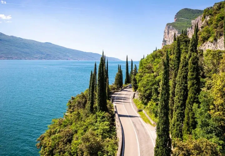 Route panoramique longeant un lac italien, idéale pour le camping-car. Cyprès élancés, falaises et eau bleue invitent à l'aventure.