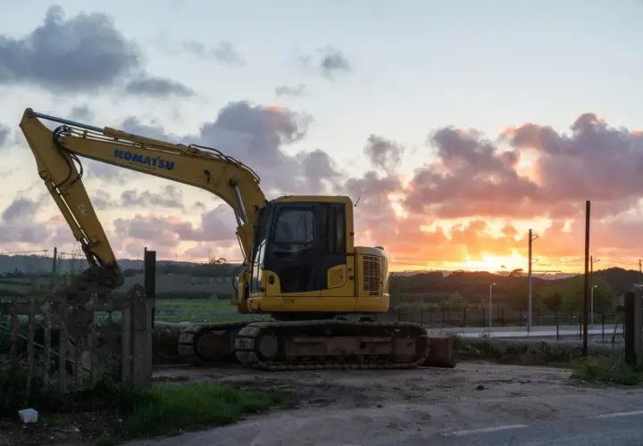 Żółta koparka Komatsu na tle zachodzącego słońca. Maszyna gotowa do pracy, nawet gdy dzień dobiega końca.