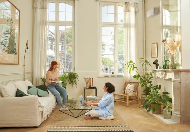 Dos mujeres disfrutan de un ambiente confortable en un salón luminoso, con el aire acondicionado en modo quiet funcionando discretamente.
