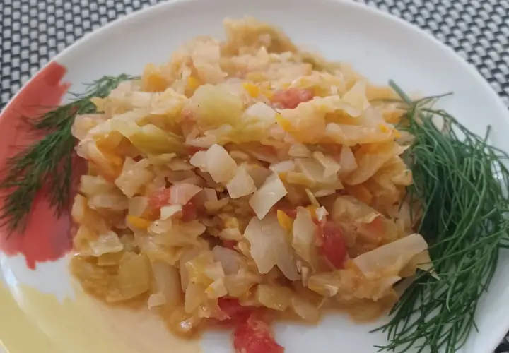 Młoda kapusta z pomidorami, duszona z koperkiem, na białym talerzu.