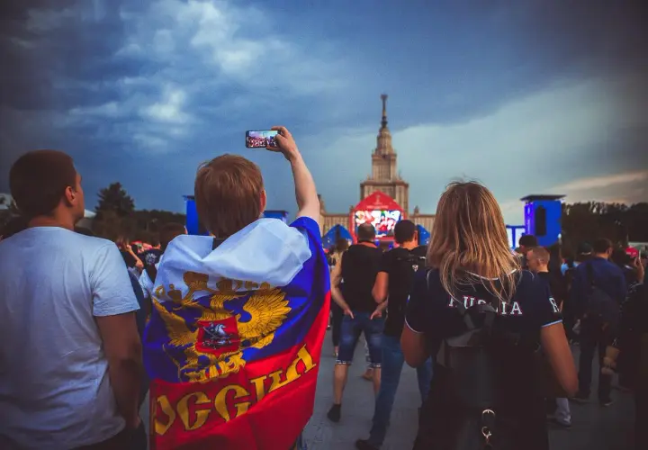 Młody kibic z flagą Rosji, wspierający klub piłkarski z Moskwy, filmuje telefonem wydarzenie przed monumentalnym budynkiem.