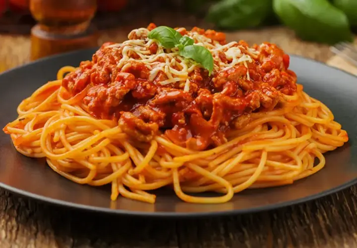 Porcja spaghetti z bogatym, mięsnym sosem bolognese, posypana startym serem i listkiem bazylii.