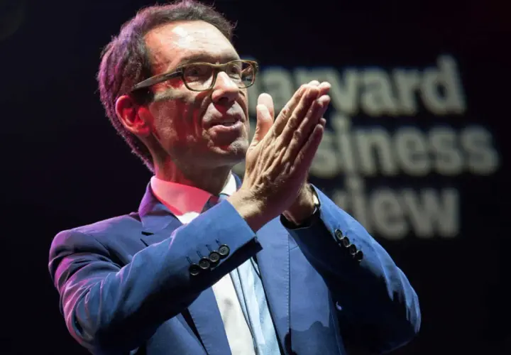 Byron Sharp, w okularach i niebieskim garniturze, z dłońmi złożonymi w geście przemowy, na tle napisu "Harvard Business Review".