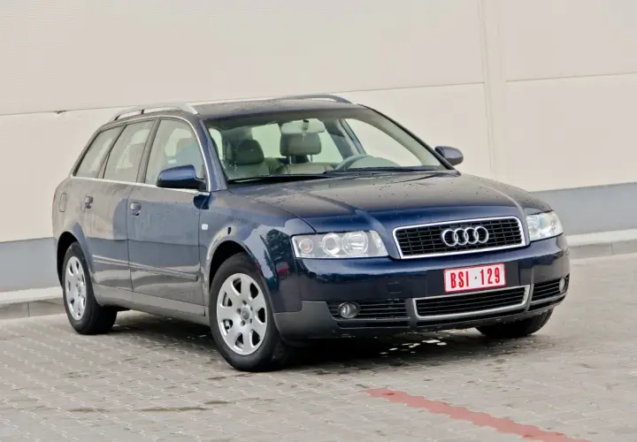 Ciemnoniebieskie Audi A4 B6 Avant na parkingu. Widać przednie reflektory i grill z logo Audi.