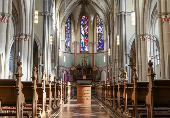 Blick in den katholischen Kircheninnenraum mit Holzbänken, Buntglasfenstern und einem Altar.