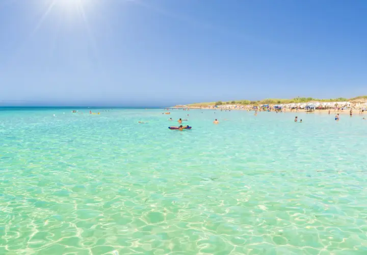 Crystal clear turquoise waters and a sandy beach with sunbathers, perfect for those wondering where to stay in Puglia for beaches.