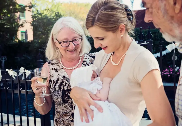Elegancka stylizacja na chrzciny: matka karmi dziecko w białej sukience, babcia z kieliszkiem wina, dziadek obok.