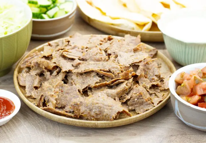 Pyszny kebab z piekarnika na talerzu, otoczony świeżymi warzywami, sosem i plackami. Idealny na domowy obiad.