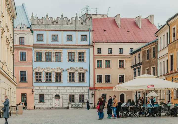Kolorowe kamienice na rynku, idealne na tani city break. Ludzie spacerują, siedzą w ogródku kawiarnianym.