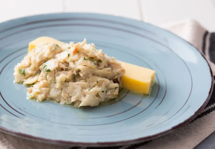 Baccalà alla Vicentina, ein cremiges Stockfischgericht mit Petersilie, serviert mit einem Stück Polenta auf einem blauen Teller.