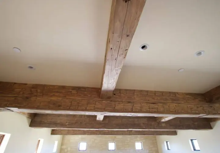Poutres apparentes en bois ciré, patinées par le temps, soutenant un plafond blanc avec des spots encastrés.