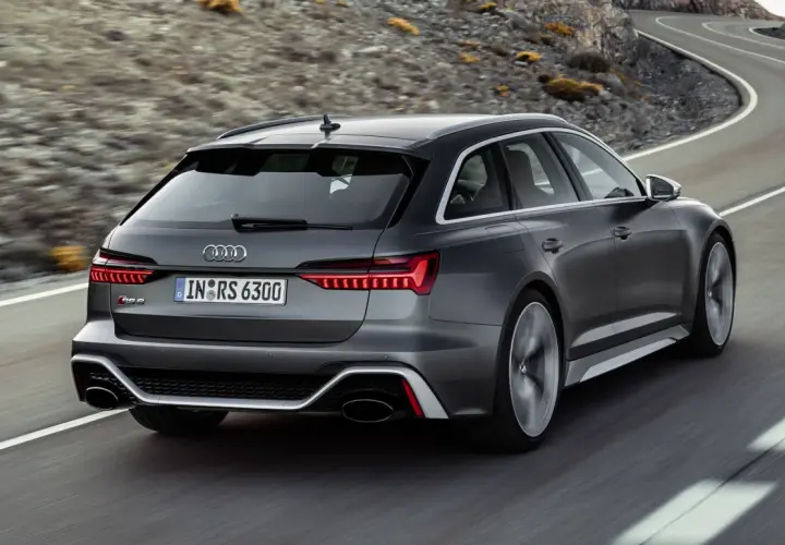 El Audi RS6 ranchera gris oscuro acelera por una carretera sinuosa entre montañas.