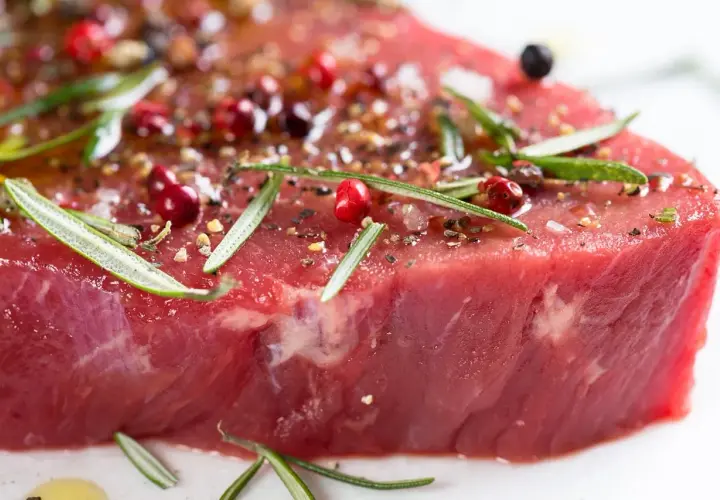 Un morceau de viande rouge, assaisonné de poivre rose, de romarin et d'épices, prêt à devenir l'une des 10 meilleurs viandes du monde.