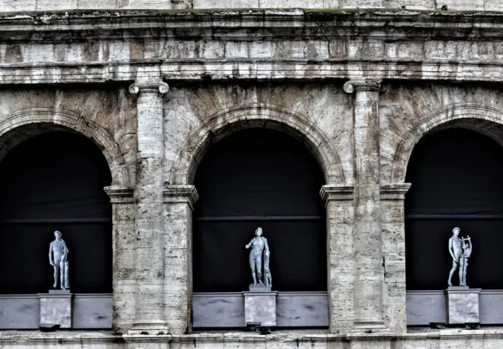 Tre statue classiche emergono dall'ombra di un imponente arco a Roma, testimoni silenziose di un passato glorioso.