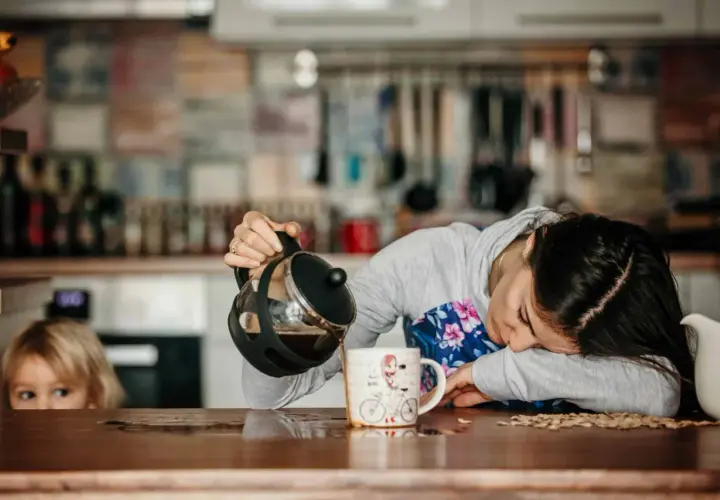 Une femme, visiblement à bout de forces, verse du café dans une tasse, le regard perdu. Un enfant la regarde, l'air intrigué. Elle semble tomber de fatigue.