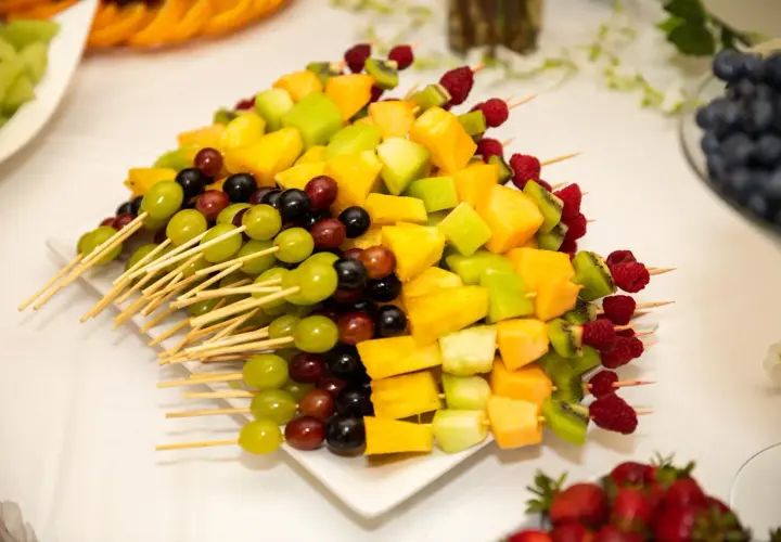 Kolorowa deska owoców na imprezę: szaszłyki z winogron, melona, kiwi, ananasa i malin.