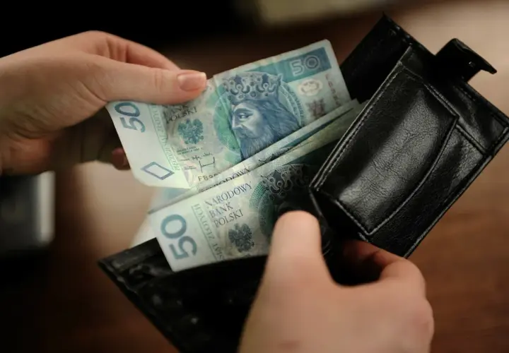 Ręce wkładają polskie banknoty 50 zł do czarnego portfela. To kieszonkowe dla dziecka na drobne wydatki.