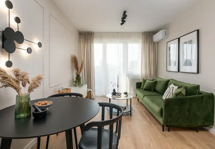 Nowoczesne mieszkanie w bloku z zieloną kanapą, czarnym stołem i designerską lampą.