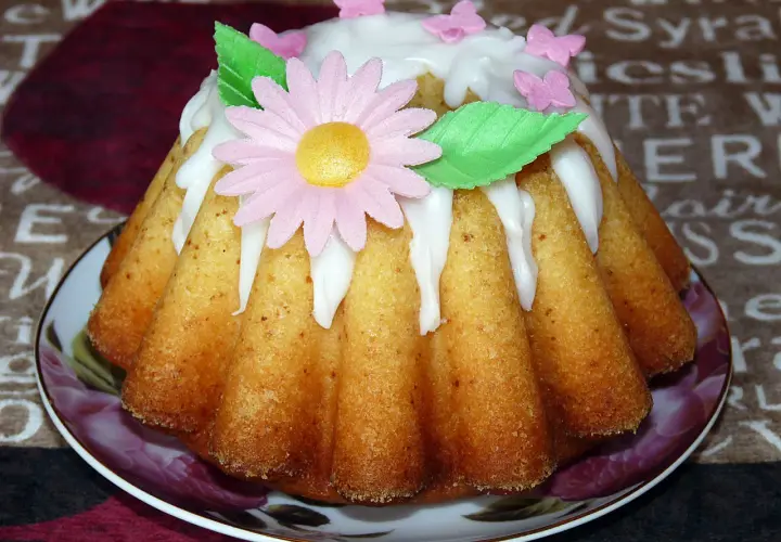 Babka jogurtowa cytrynowa ozdobiona lukrem, różowym kwiatkiem i motylkami. Idealna na wiosenne popołudnie.