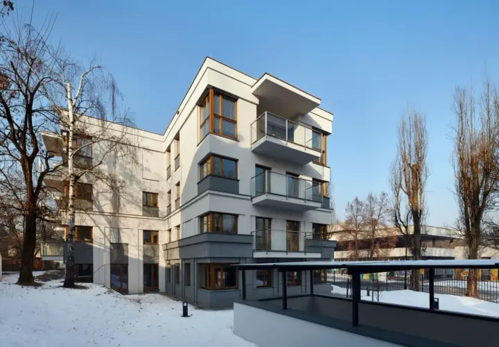 Nowoczesne osiedle oficerskie Kraków, z białymi fasadami i drewnianymi oknami, otoczone zimowym krajobrazem i nagimi drzewami.
