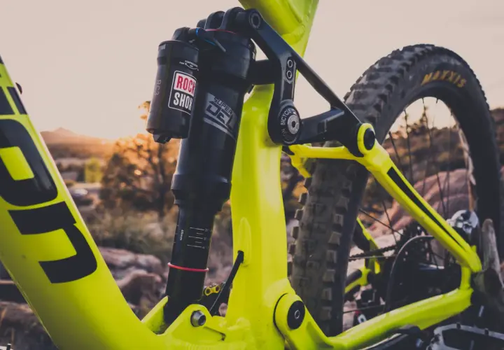 Close-up of a bright yellow mountain bike's rear suspension. The Rock Shox Super Deluxe shock has a length chart visible.