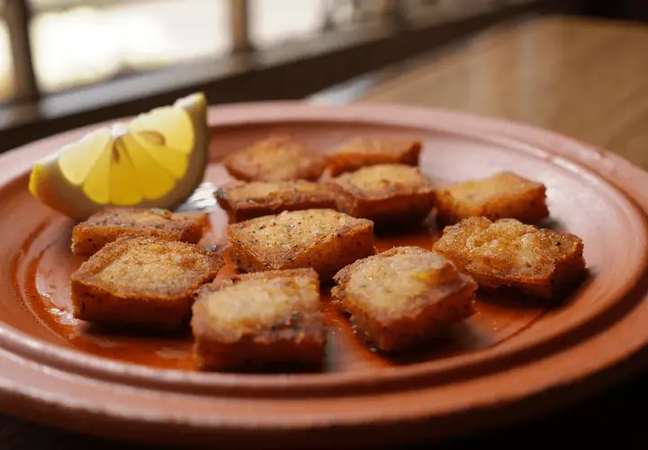 Bocaditos dorados de bacalao rebozado, crujientes y listos para disfrutar, acompañados de una rodaja de limón fresco.