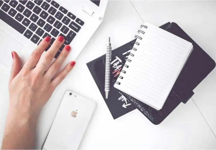 Karta pracy na biurku: dłoń na klawiaturze laptopa, obok telefon, notatnik i długopis.