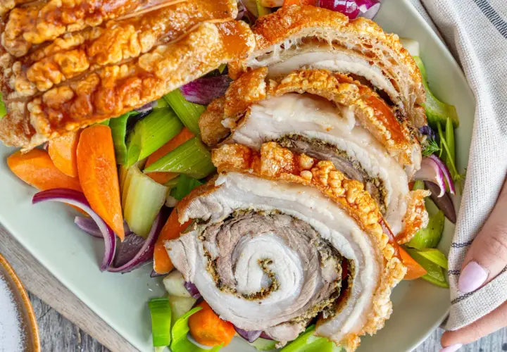 Knusprige Porchetta, ein italienischer Schweinebraten, wird mit karamellisierten Karotten, Sellerie und roten Zwiebeln serviert.