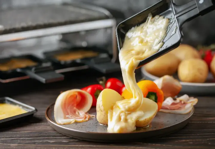 Formaggio fuso in padella, filante e dorato, viene versato su patate e salumi. Un piatto invitante e gustoso.