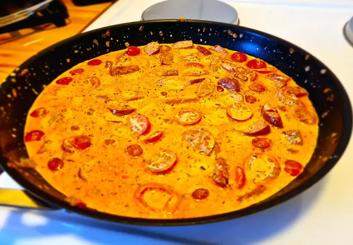 En krämig korv stroganoff deluxe i en stekpanna, med skivad korv och körsbärstomater i en gyllene sås.