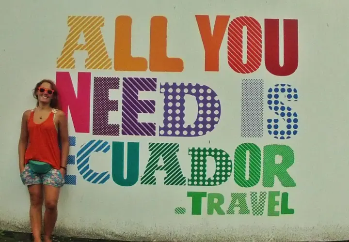 Uśmiechnięta turystka w Vilcabamba pozuje na tle kolorowego napisu "All you need is Ecuador. Travel".