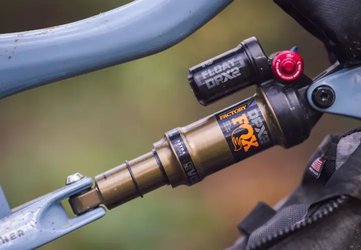 Close-up of a blue bicycle frame with a gold and black Fox Float DPX2 Factory shock. The shock has "FACTORY" and "DPX2" branding.