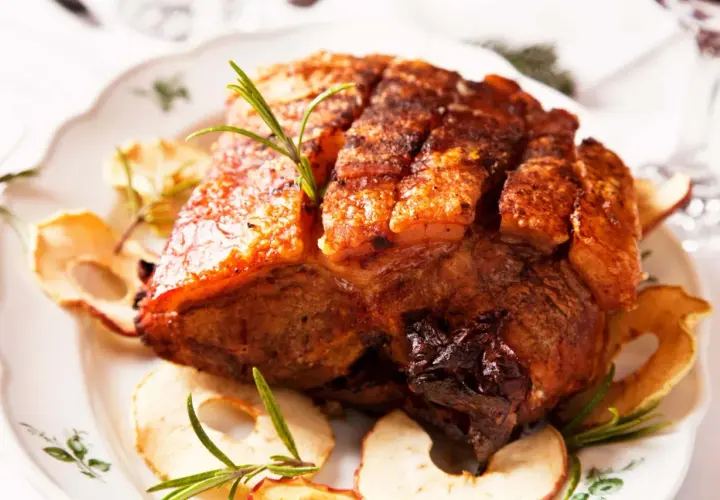 Ein knuspriger Krustenbraten aus dem Backofen, garniert mit Rosmarin und Apfelringen auf einem festlichen Teller.