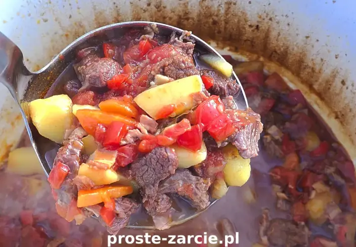 Gulasz z kociołka żeliwnego na ognisku, pełen mięsa, ziemniaków i warzyw, paruje apetycznie.