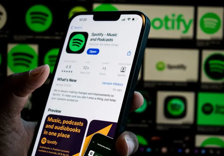 Dłoń trzyma smartfon z otwartą aplikacją Spotify. W tle widać ikony Spotify.