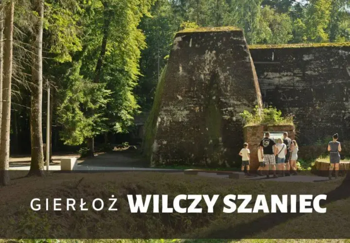Grupa turystów zwiedza historyczny Wilczy Szaniec w Gierłoży, podziwiając potężne bunkry w otoczeniu zieleni.