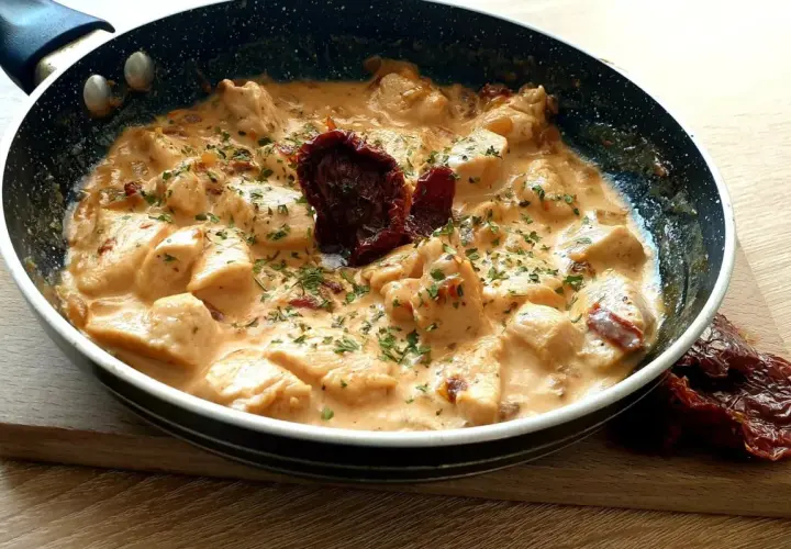 Kawałki kurczaka w kremowym sosie z suszonymi pomidorami i natką pietruszki. Danie "marry me chicken" wygląda apetycznie.