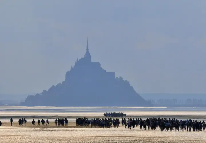 Silhouetten von Menschen auf dem Wattboden, die sich dem majestätischen Mont Saint-Michel nähern.