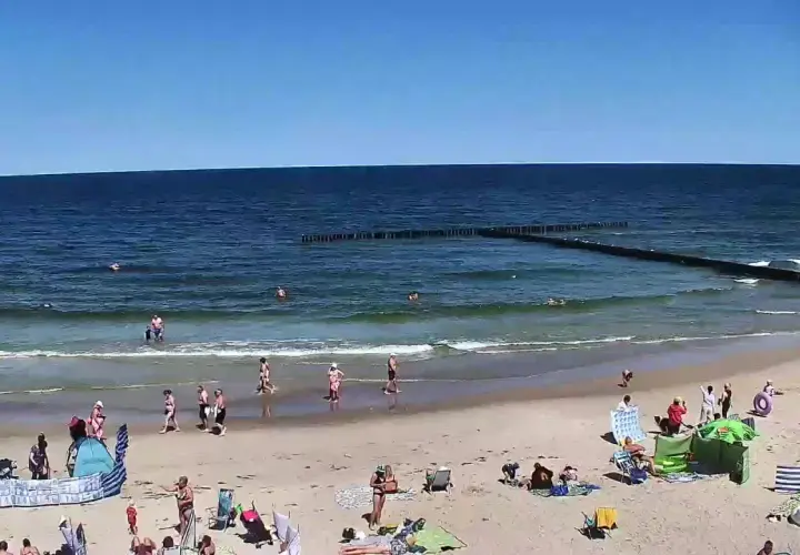 Słoneczna plaża w Dźwirzynie, ludzie kąpią się w morzu i odpoczywają na piasku. To jedne z wielu atrakcji tego miejsca.