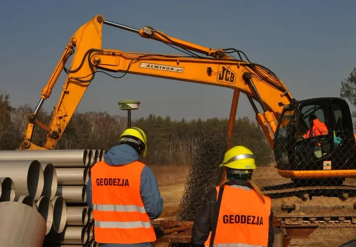 Geodeci w kamizelkach obserwują pracę koparki. Zastanawiasz się, ile kosztuje wynajem koparki?