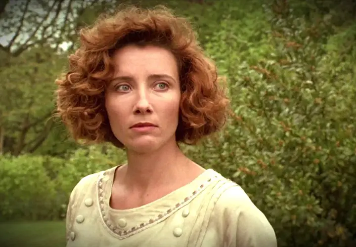Emma Thompson w filmie, z burzą rudych loków i w jasnej sukni, spogląda zamyślona na tle zieleni.