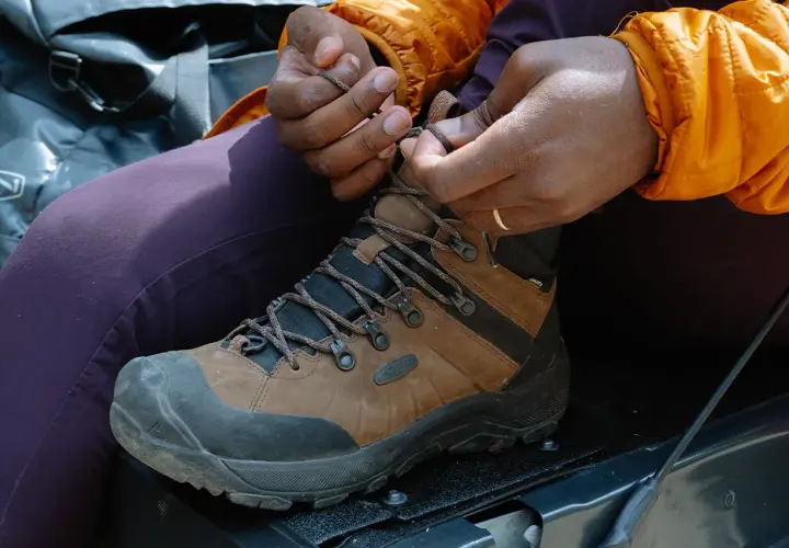 Close-up of hands tying brown hiking boots, demonstrating how to tie hiking boots for an outdoor adventure.