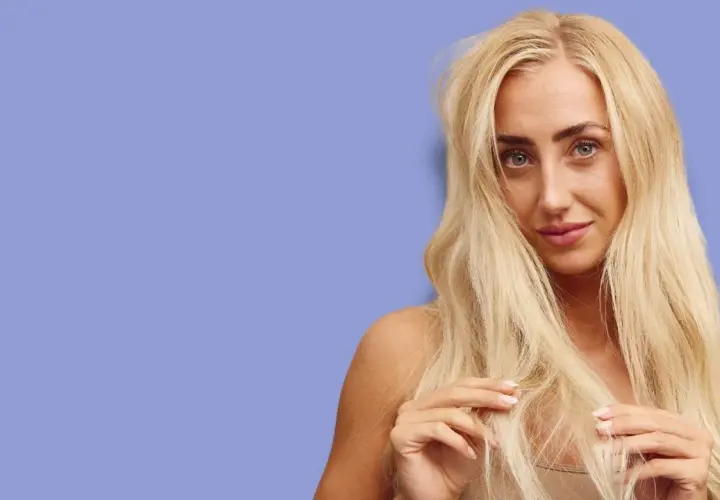 Blond kvinna med långt, tjockt hår som verkar ha hög porositet. Hon rör vid sitt hår med fingrarna.