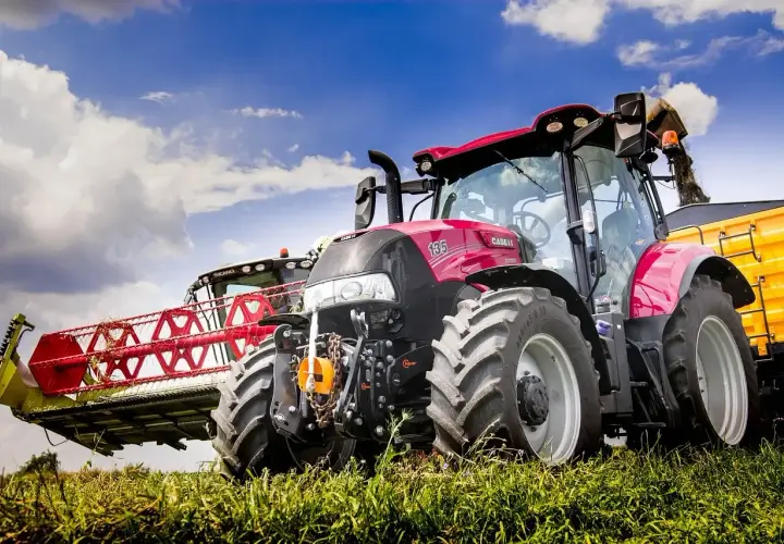 Czerwony traktor Case IH z hederem żniwnym i żółtą przyczepą. Warto wiedzieć, jak wymienić olej w takim sprzęcie, by służył latami.