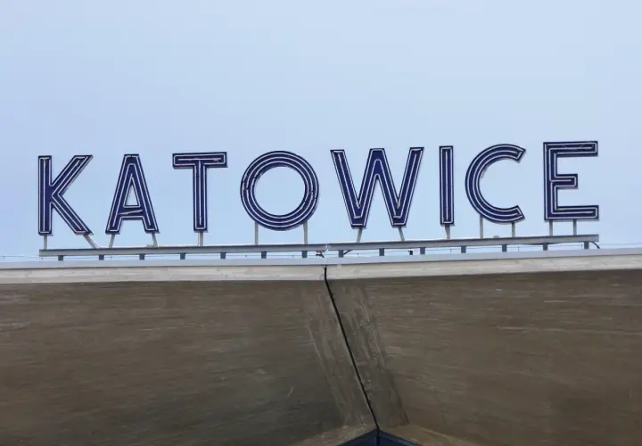 Napis "KATOWICE" z niebieskimi neonami na tle jasnego nieba.